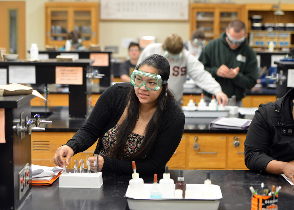 A chemistry student smiles while wearing safety goggles